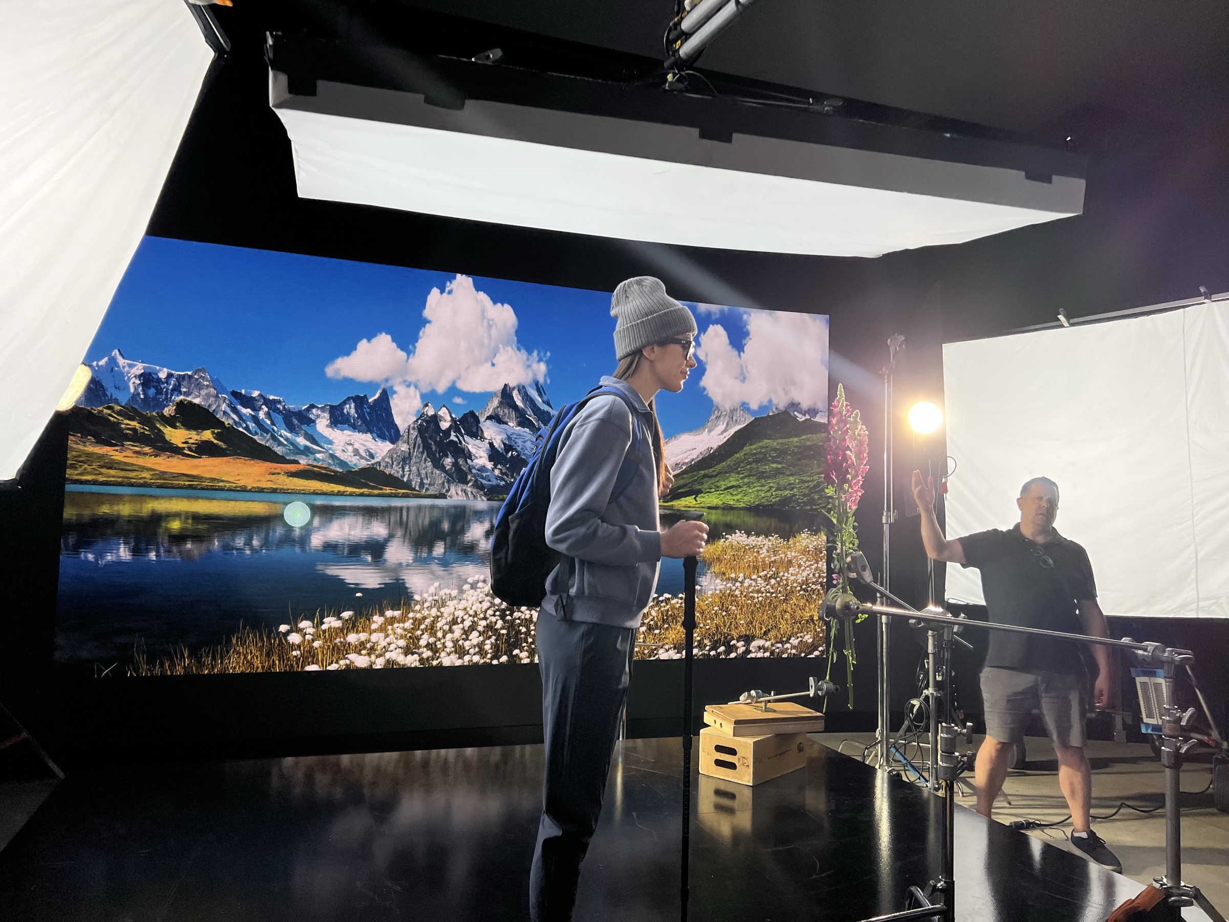 Behind-the-scenes of Qualcomm XR shoot — talent wearing smart glasses and backpack on LED volume stage with alpine mountain lake landscape displayed on curved LED video wall