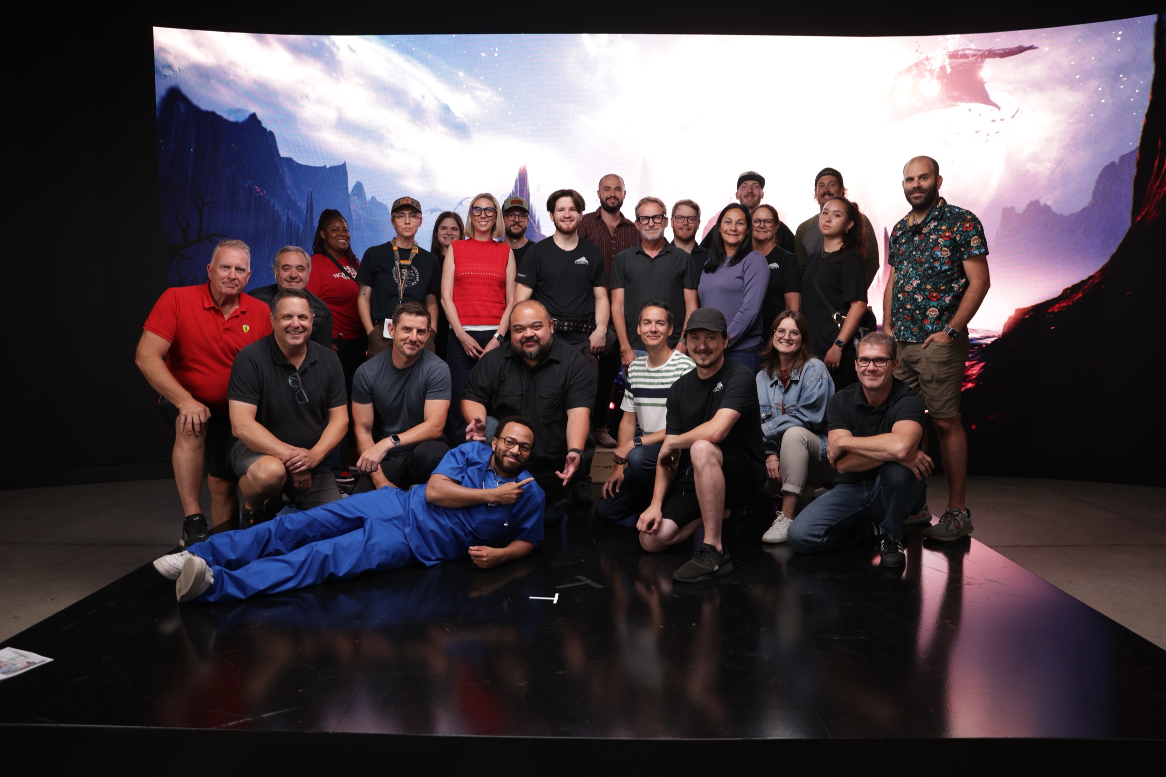 Full cast and crew group photo from Qualcomm XR virtual production shoot — 25 team members posed on LED volume stage floor with curved LED wall displaying fantasy landscape behind them