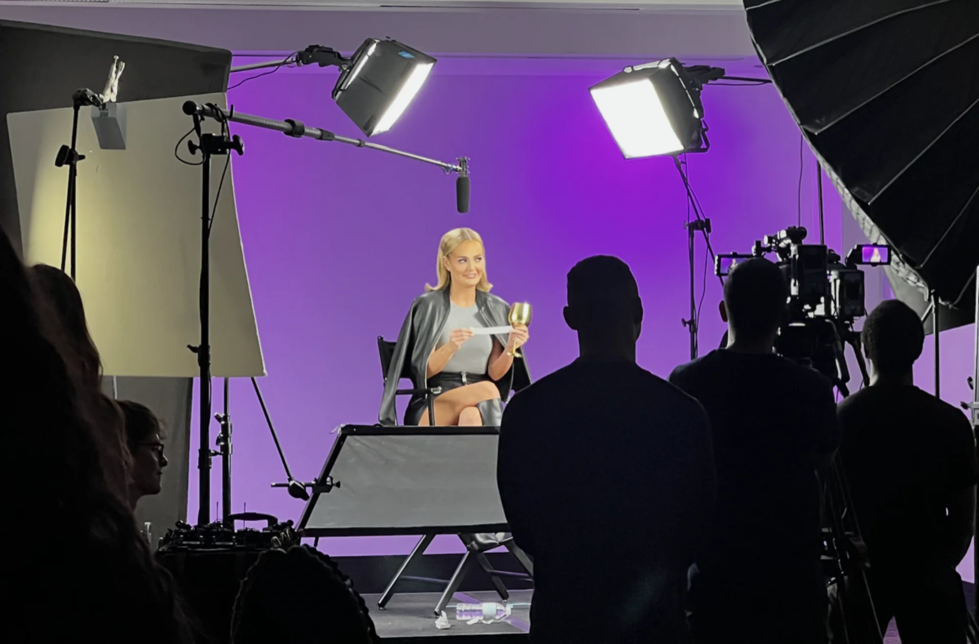 Behind the scenes — talent on purple cyclorama with full crew, boom, lighting, and cameras